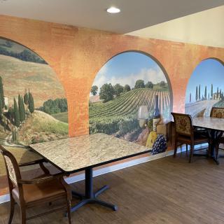 A cozy restaurant interior featuring a scenic mural depicting a countryside landscape, with tables and chairs arranged for dining.