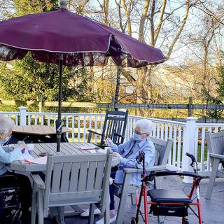Two seniors sitting outdoors on a patio, enjoying a sunny day under a large umbrella.