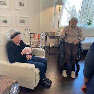 Two elderly individuals engaged in a moment together in a cozy indoor space.