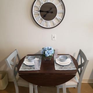 A cozy dining setup with a round table for two, complete with place settings and a decorative clock on the wall.