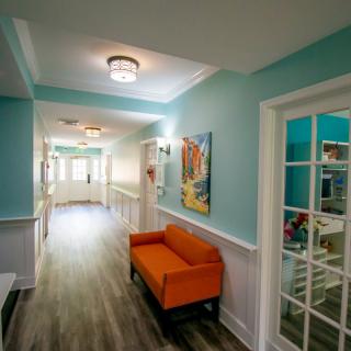 A bright and cheerful hallway with an orange sofa and artwork on the walls, illuminated by natural light.