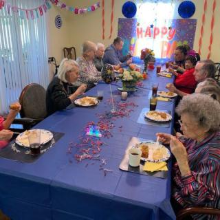 A group of elderly people enjoying a festive birthday celebration with food and decorations.