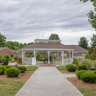 A landscaped garden leads to a building with a gazebo structure in front.