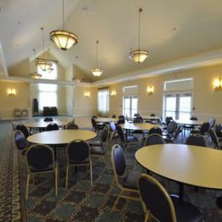 A spacious conference room with round tables and chairs, well-lit by overhead lighting and natural light from windows.