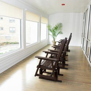 A serene sunroom with wooden rocking chairs aligned by large windows, allowing abundant natural light to fill the space.