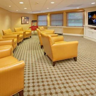 A bright and comfortable waiting room with yellow armchairs, carpeting, and a wall-mounted television.