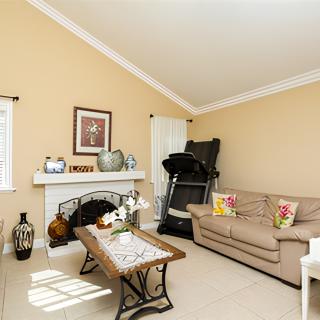 A cozy living room with a beige color scheme, featuring a sofa, coffee table, treadmill, and decorated fireplace.