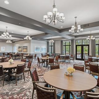 A spacious dining room with multiple round tables, chairs, and elegant chandeliers.