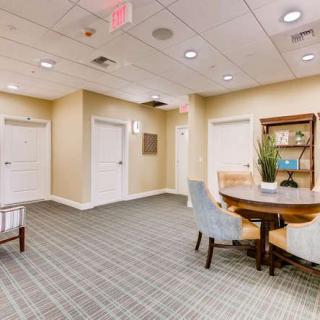 A modern waiting area featuring a round table with chairs, a plant centerpiece, and a bookshelf in the background.