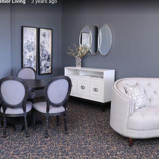 A stylish living room with gray walls, featuring a round dining table, upholstered chairs, decorative mirrors, and a white couch.