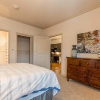 A cozy bedroom featuring a neatly made bed, wooden dresser with decor, and two open doorways.