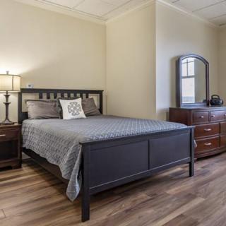 A cozy bedroom with a modern bed and matching furniture, featuring a nightstand, dresser, and mirror on wooden flooring.