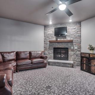 A cozy living room with a stone fireplace, leather couch, and ceiling fan.