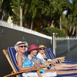 Three elderly women relaxing on deck chairs by the pool, enjoying a sunny day.
