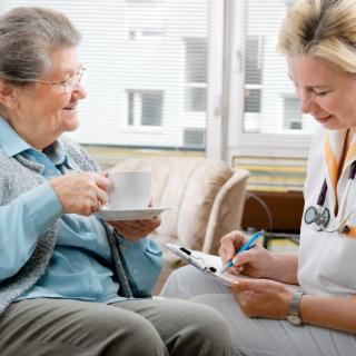 A healthcare professional consults with an elderly patient over a cup of tea.