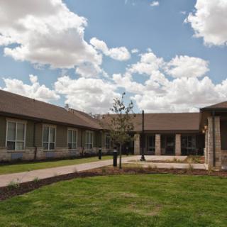 A serene view of a modern building surrounded by lush greenery and a partly cloudy sky.