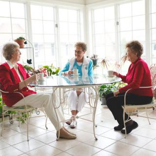 Three senior women enjoying a conversation over tea in a bright, sunlit room.