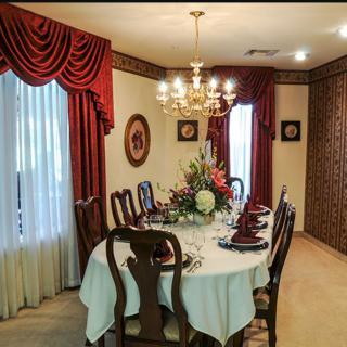 A formal dining room with an elegantly set table, complete with a floral centerpiece and lit chandelier.