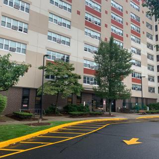 View of a high-rise apartment building with trees and a parking lot in the foreground.