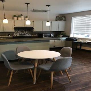 A modern kitchen and dining area with a round table and chairs, featuring pendant lights and wood flooring.