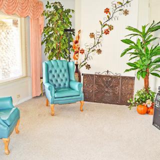A cozy living room with teal chairs, lush plants, and floral wall decor.