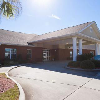 A sunny day view of a brick building with a covered entrance and circular driveway.