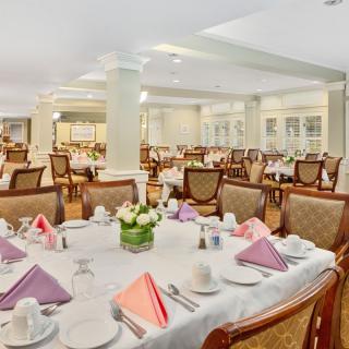 An elegant dining room with tables set for guests, featuring folded napkins and floral centerpieces.
