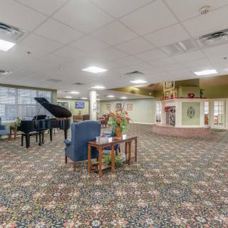 A spacious lobby area featuring a grand piano, comfortable seating, and decorative floral arrangements on a patterned carpet.