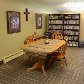 A cozy dining area featuring a wooden table surrounded by chairs, decorated with a tablecloth and accompanied by a bookshelf filled with various items.