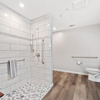 A modern, accessible bathroom with white tiled shower and wood-style flooring.