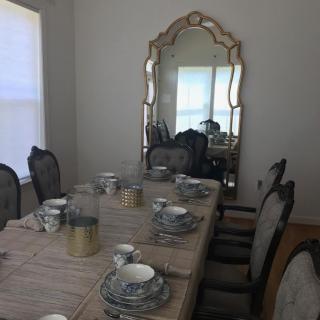 A dining room with an elegantly set table, featuring a large mirror and upholstered chairs.