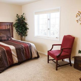 A cozy and simple bedroom with a bed, red chair, and large window.