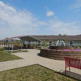 A tranquil garden area with a fountain, surrounded by a pathway and benches under a sunny sky.