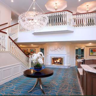 A luxurious hotel lobby featuring a grand chandelier, elegant staircase, and cozy fireplace.