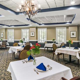 An elegant restaurant dining room featuring neatly set tables, a chandelier, and decorative flowers.