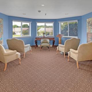 A cozy living room with multiple armchairs, a desk, and large windows allowing natural light.