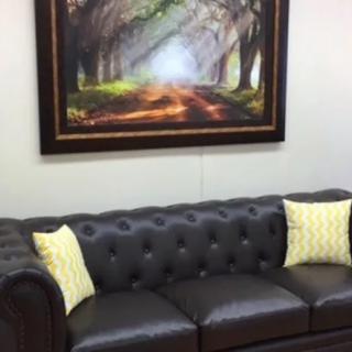 A cozy living room setup with a leather sofa, decorative pillows, and a framed painting on the wall.