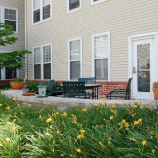 A serene outdoor patio area with seating and blooming flowers in front of an apartment building.