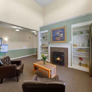 A cozy living room with a fireplace, surrounded by chairs and decorated shelves.