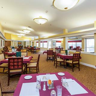 A spacious dining area with neatly arranged tables and chairs, featuring overhead lighting and a carpeted floor.