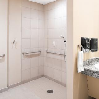 An accessible bathroom featuring a shower area with handrails and a sink.
