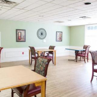 A bright and spacious dining area with several tables and chairs, featuring green walls, a clock, and wall art.