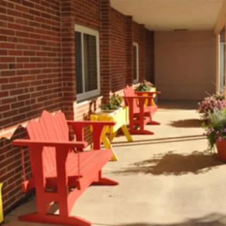 A bright patio with red and yellow chairs against a brick wall, adorned with potted plants.