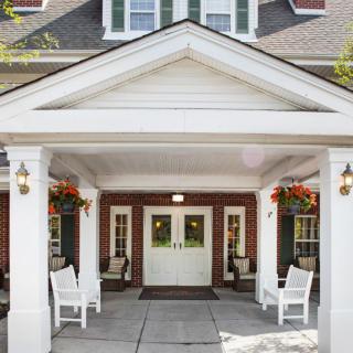 A welcoming porch entrance with white chairs and hanging flowers.
