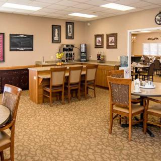 A cozy cafe with a coffee station, tables, and chairs, featuring framed pictures on the walls.