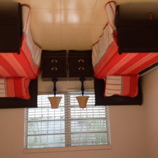 A neatly arranged bedroom with twin beds featuring striped bedding, flanked by nightstands and lamps, positioned near a window with curtains.