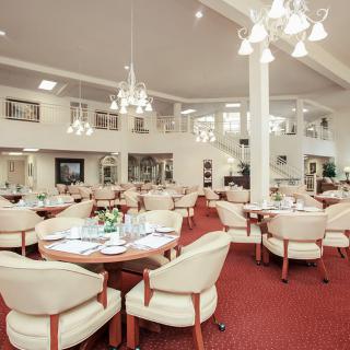 A spacious dining room with elegant chandeliers and neatly arranged tables and chairs.