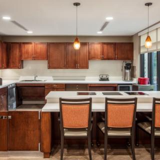 A modern kitchen with wooden cabinets and an island featuring bar stools and pendant lighting.
