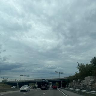A view of a highway under a cloudy sky, with vehicles traveling and an overpass visible.