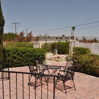 A patio with metal chairs and a table, surrounded by a garden and bushes.